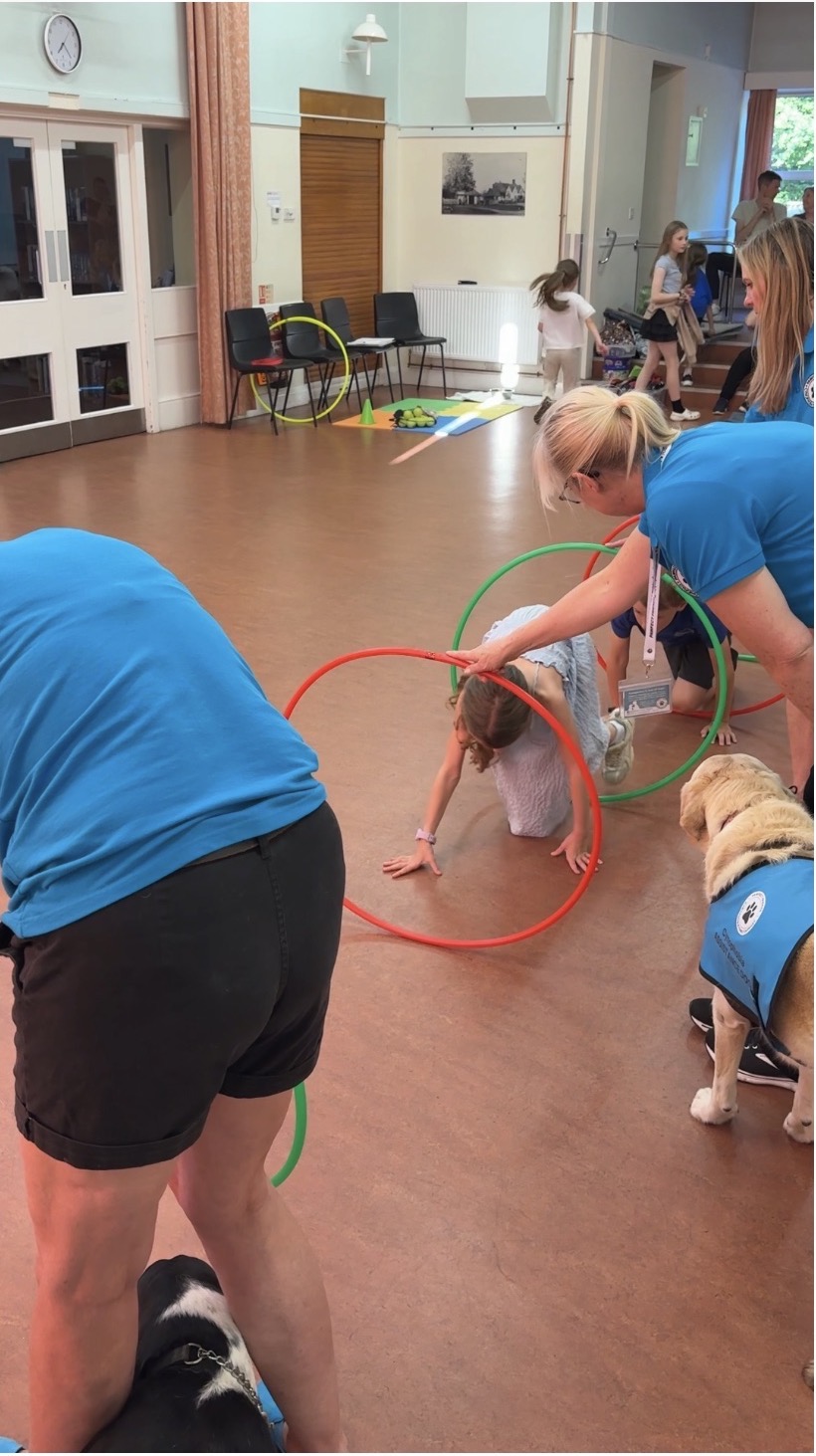 Child crawling through hula hoops alongside a dog in blue vest during a fun agility exercise in class
