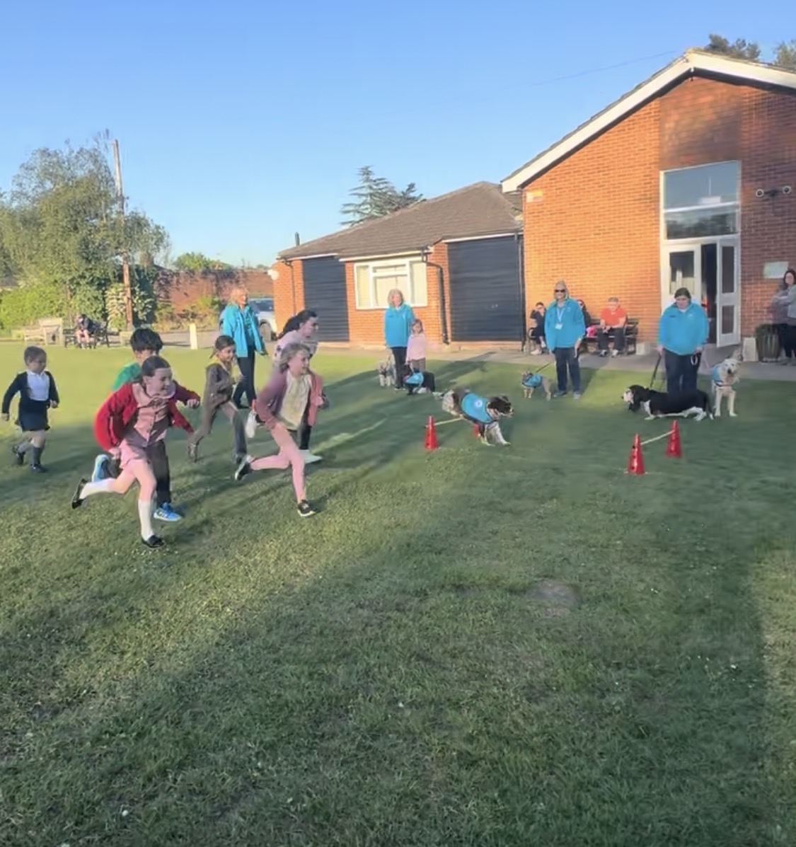 Children racing across the playing field during an outdoor session with handlers and dogs lined up behind
